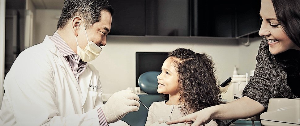 Dentist examining a smiling young patient while her mother looks on